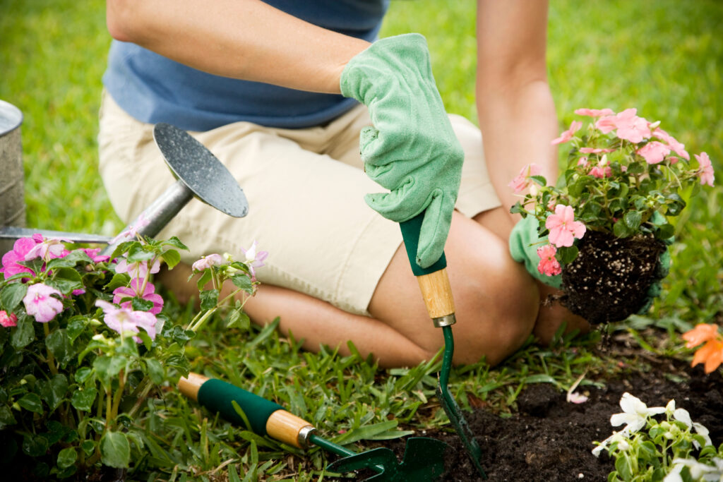 A person sits on the grass, surrounded by flowers, with a small trowel for gardening.