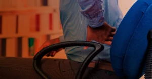 A close-up shot of a man sitting on his desk chair and holding his lower back in pain.
