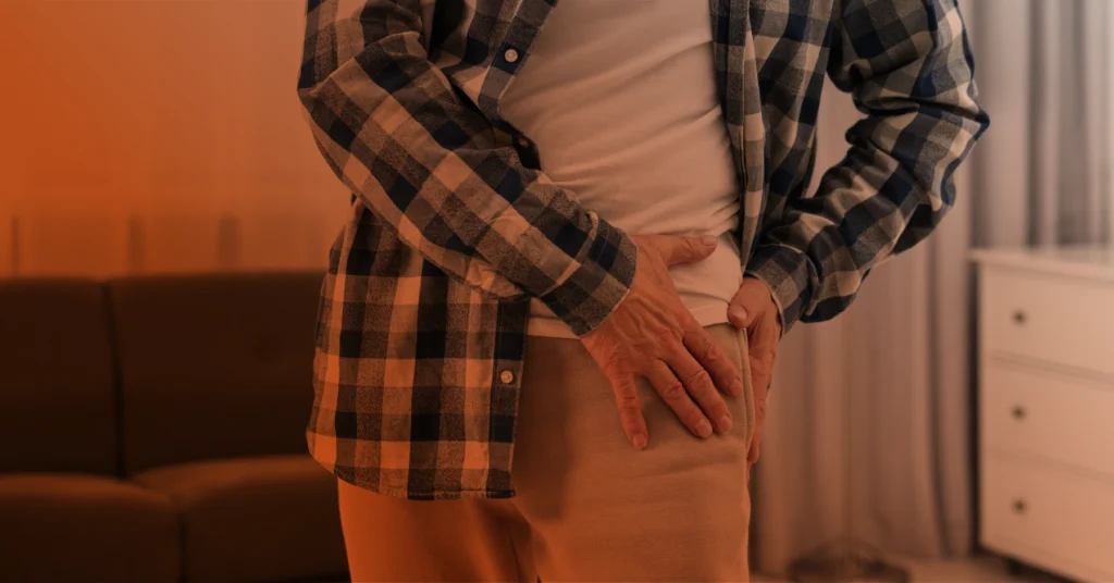 A close-up shot of a man holding his hip in pain.